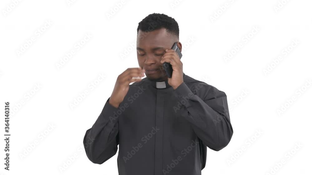 Portrait of young African priest talking on the phone, holding it in left hand and frustrated by bad news isolated on white background Portrait of young African priest talking on the phone, holding it in left hand and frustrated by bad news isolated on white background