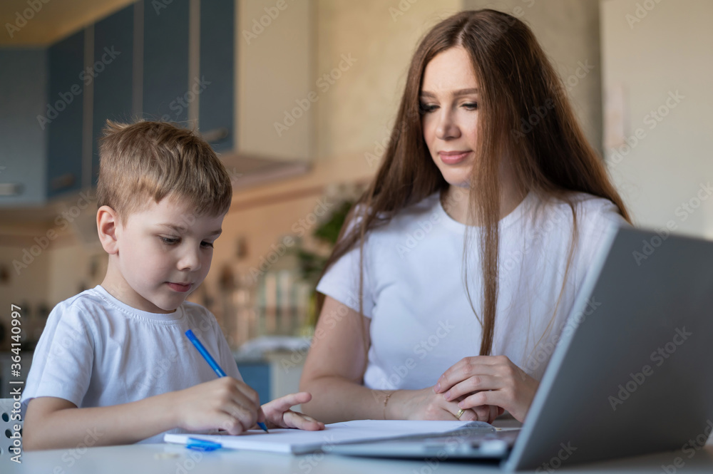 Caucasian woman helps her son learn lessons. Caring mother checks the child's homework. Study at home during quarantine. Caucasian woman helps her son learn lessons. Caring mother checks the child's homework. Study at home during quarantine.