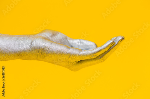 Elegant female hand with a silver paint on it shows open palm, isolated on a yellow background. Free space for text