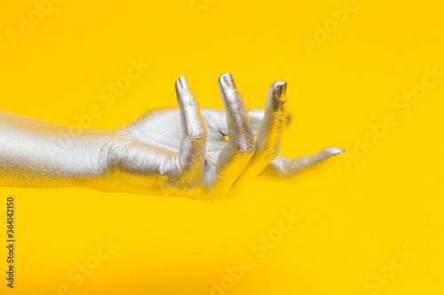 Fototapeta Naklejka Na Ścianę i Meble -  Elegant female hand with a silver paint on it isolated on a yellow background. Free space for text