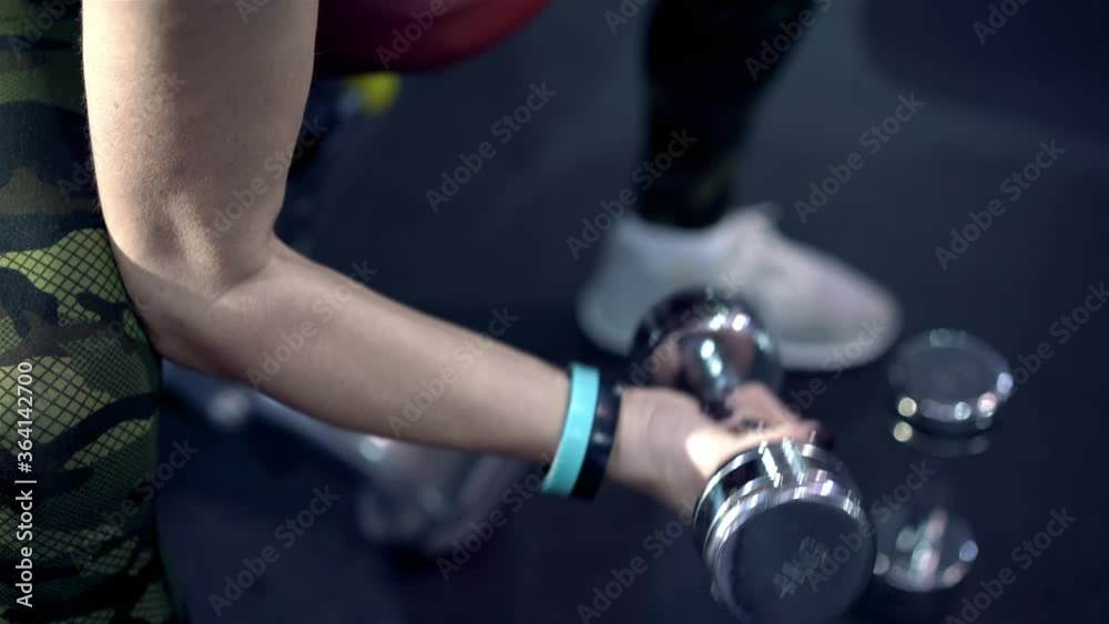 Close-up raised arms of middle-aged woman lifting dumbbells. Lady of thirty training her body in gym. Active woman exercising in fitness hall. Woman doing sports and fitness training. Leisure concept. Close-up raised arms of middle-aged woman lifting dumbbells. Lady of thirty training her body in gym. Active woman exercising in fitness hall. Woman doing sports and fitness training. Leisure concept.
