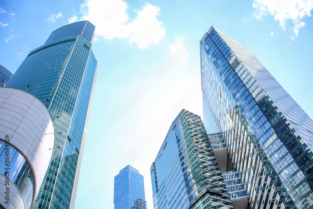 Low angle view of large skyscrapers covered with glass. Blue sky with some white clouds in the background. Modern office buildings theme. Low angle view of large skyscrapers covered with glass. Blue sky with some white clouds in the background. Modern office buildings theme.