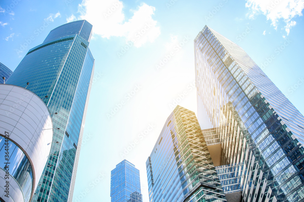 Low angle view of large skyscrapers covered with glass. Blue sky with some white clouds in the background. Modern office buildings theme.