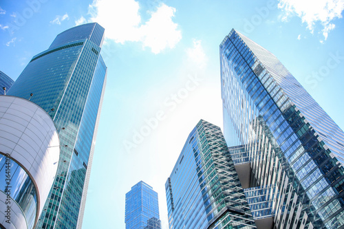 Low angle view of large skyscrapers covered with glass. Blue sky with some white clouds in the background. Modern office buildings theme.