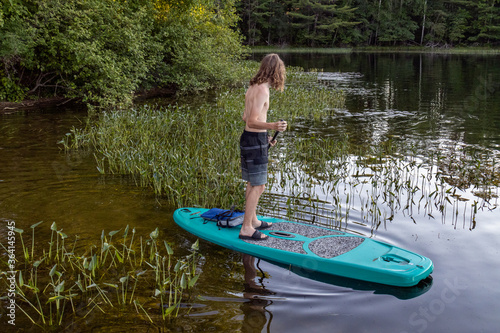 teenage boy paddle boarding in reeds on lake