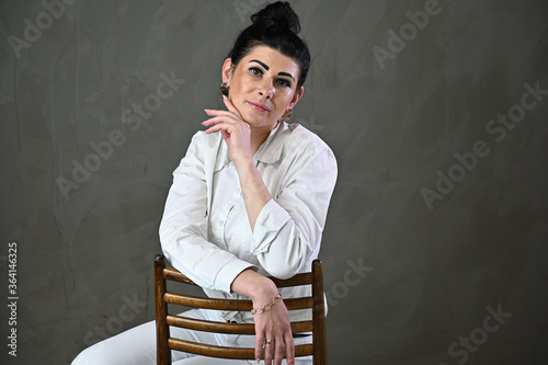 Stylish studio portrait of a caucasian brunette woman sitting on a chair on a gray background