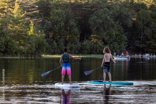 Fototapeta Naklejka Na Ścianę i Meble -  two teenage boys paddle boarding on lake