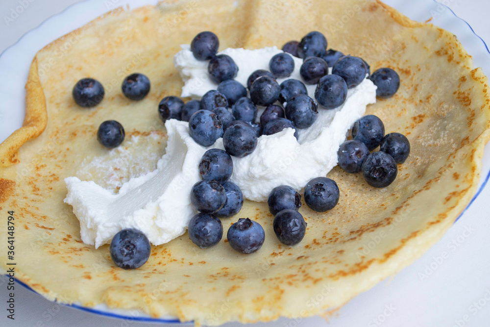 Artistic composition in natural daylight. Homemade pancake with blueberries and curd cheese (focus on the filling, the edge of the pancake is specially blurred)