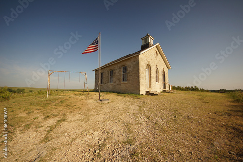 Old one-room school house, swing set and flag in the Kansas countryside.