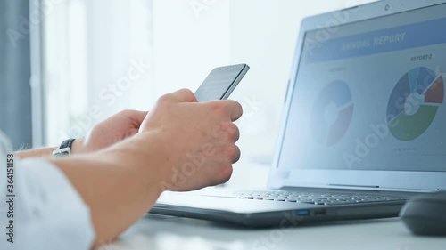 Trader Man Using Cellphone And Checks Report Data On Laptop Computer. Finance And Trade Concept.