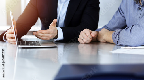 Business people using laptop computer while working together in sunny modern office. Unknown businessman with colleague at workplace. Teamwork and partnership concept
