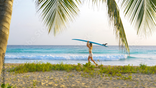 Young woman on fun surfing trip in Barbados carries a surfboard on her head.