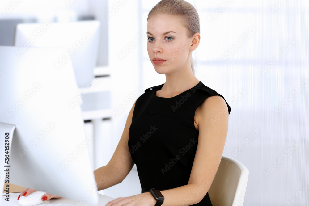 Business woman working with computer while sitting at the desk in modern office. Secretary or female lawyer looks beautiful in black dress. Business people concept