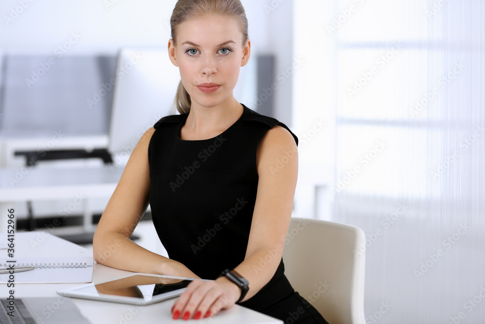 Business woman working with tablet computer while sitting at the desk in modern office. Secretary or female lawyer looks beautiful in black dress. Business people concept