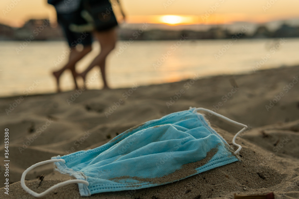 A used disposable mask (protect from COVID-19, Coronavirus) is on a beach, covered with sand, leading to bad consequences like pollution or contamination of the nature and water A used disposable mask (protect from COVID-19, Coronavirus) is on a beach, covered with sand, leading to bad consequences like pollution or contamination of the nature and water