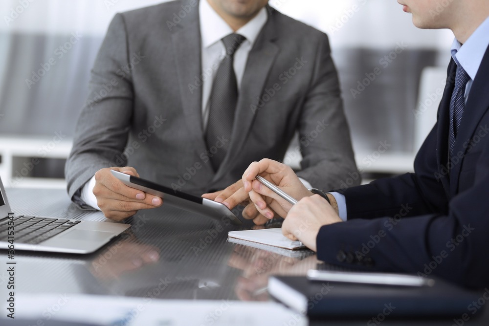 Unknown businessman using tablet computer and working together with his colleague while sits at the glass desk in modern office. Teamwork and partnership concept Unknown businessman using tablet computer and working together with his colleague while sits at the glass desk in modern office. Teamwork and partnership concept