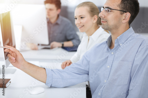 Business people working together in modern office. Happy smiling adult businessman using pc computer with colleagues. Teamwork and partnership concept