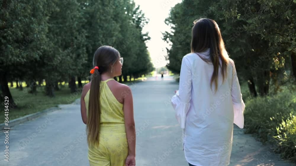 Woman with daughter teenager walk in the park. Happy family - mom and daughter