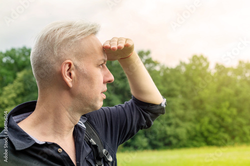 the gray-haired man, closing his eyes with his hand from the sun, looks into the distance. blurred background. High quality photo