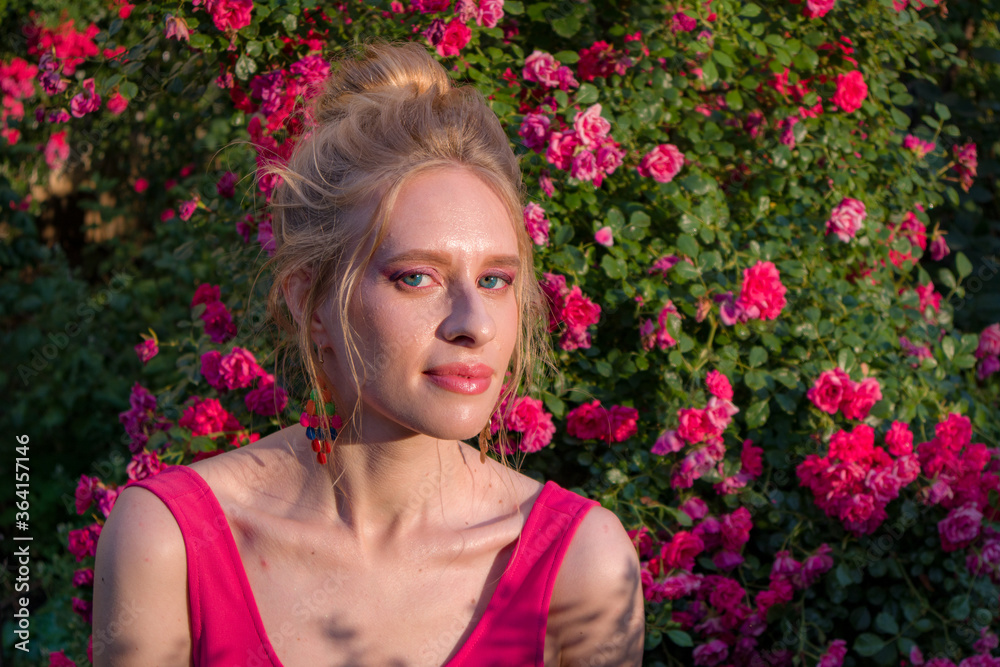 blonde with curly hair and beautiful makeup in a dress on a background of blooming roses blonde with curly hair and beautiful makeup in a dress on a background of blooming roses