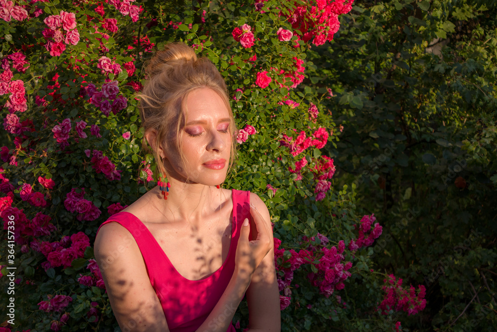 blonde with curly hair and beautiful makeup in a dress on a background of blooming roses blonde with curly hair and beautiful makeup in a dress on a background of blooming roses