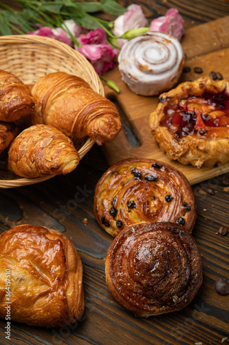 Assorted pastries, croissants, buns. On a brown wooden table.
