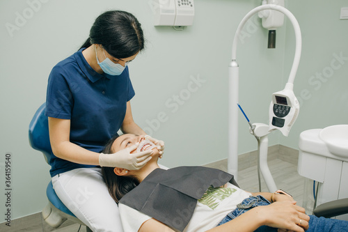 Female dentist in medical white latex gloves puts rubber dam on a patient in a dental clinic. Cleaning teeth. Modern dental office photo