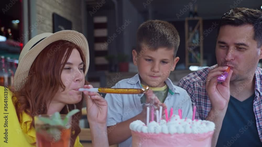 cheerful parents with horns celebrate birthday with their son, little cute boy has fun at festive party and blows out candles on cake while enjoying spring in cafe or restaurant with his family cheerful parents with horns celebrate birthday with their son, little cute boy has fun at festive party and blows out candles on cake while enjoying spring in cafe or restaurant with his family