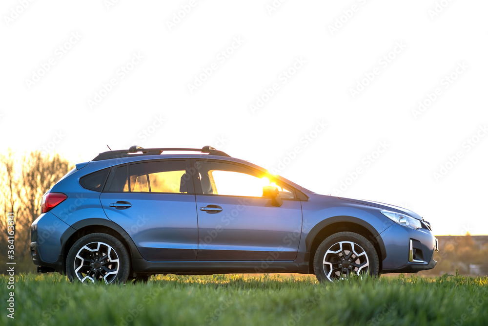 Landscape with blue off road car on green grass at sunset. Traveling by auto, adventure in wildlife, expedition or extreme travel on a SUV automobile. Offroad 4x4 vehicle in field at sunrise.