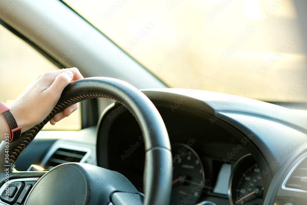 Close up view of woman hands holding steering wheel driving a car on city street on sunny day.