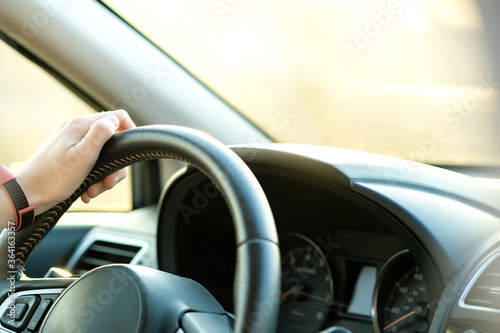 Close up view of woman hands holding steering wheel driving a car on city street on sunny day. © bilanol