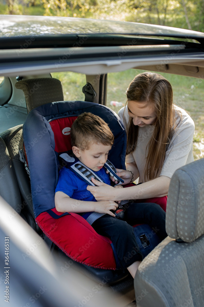 Happy mother looking at her son in a baby seat. Young female preparing kid for a trip. Safety driving concept Happy mother looking at her son in a baby seat. Young female preparing kid for a trip. Safety driving concept