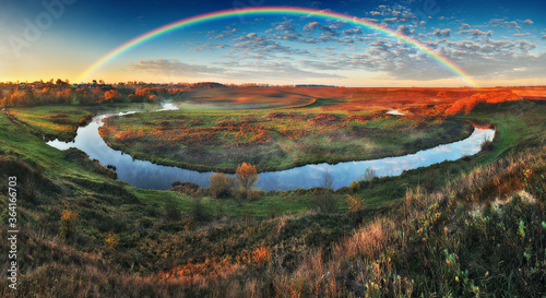 Amazing rainbow over the small rural river. autumn morning