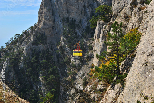 The cable car goes up the mountain on a sunny day. Yellow cabin against the background of the mountains and the sky.
