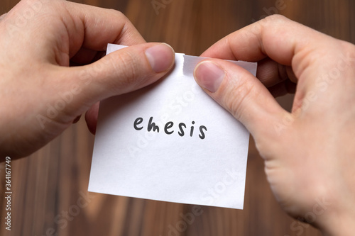 Hands of a man tearing a piece of paper with inscription emesis photo