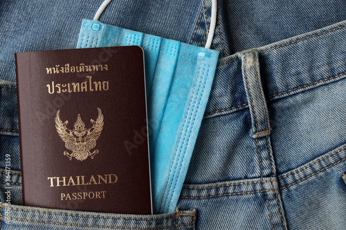 Tourism and traveling concept in New Normal after Covid-19 / Coronavirus pandemic. Thai Passport travel with medical mask in jeans pocket with copy space.