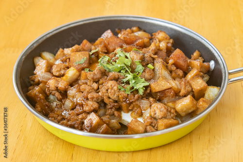Stir Fried Pork with Onion and Garlic and Black Soy Sauce and Coriander Topping and Tofu in Pan on Wood Table with Natural Light