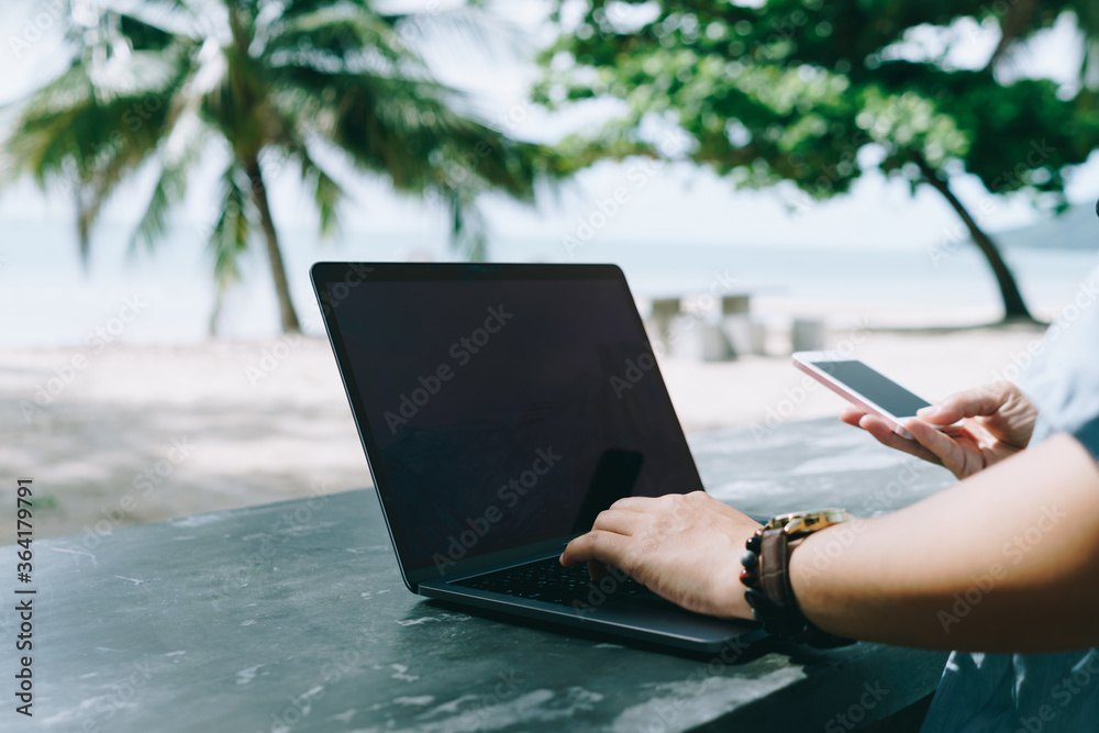 Obraz premium Woman using laptop and smartphone to work study in vacation cady at beach background.