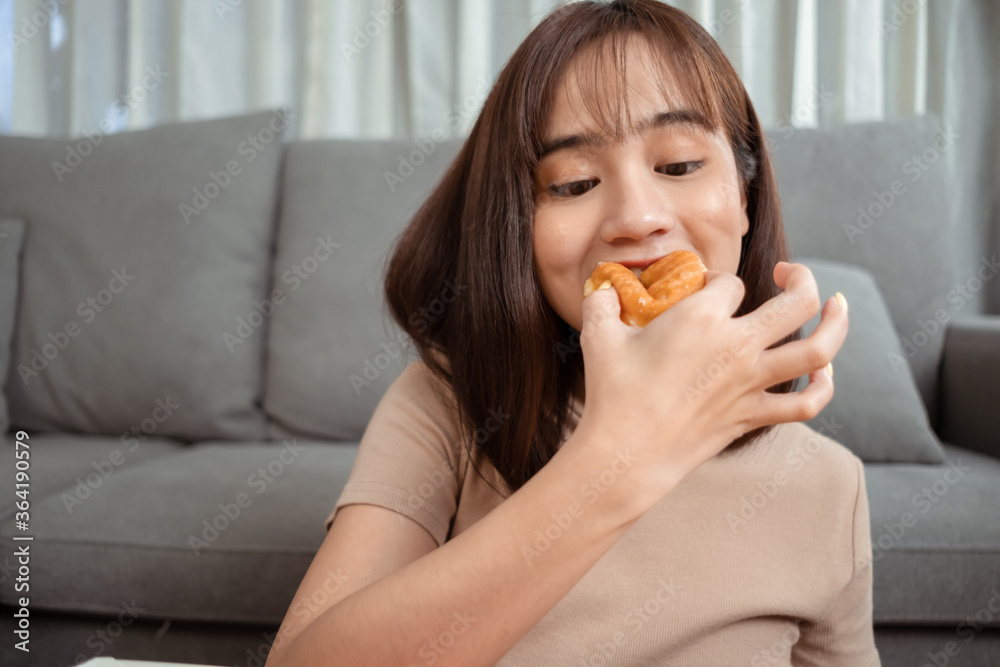 Young asian woman takeaway eating donut junk food on couch in living room Young asian woman takeaway eating donut junk food on couch in living room
