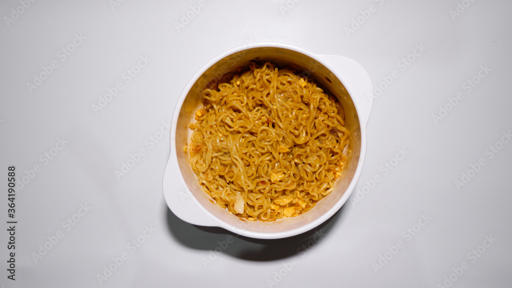 A tasty instant fried noodle (Indomie Goreng) mixed with scrambled boiled egg in a white bowl. Top view of delicious fried noodle A tasty instant fried noodle (Indomie Goreng) mixed with scrambled boiled egg in a white bowl. Top view of delicious fried noodle