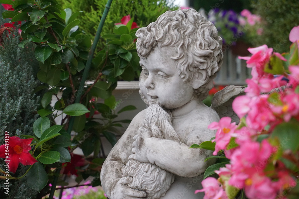 Statue of a cupid, angel holding a doll in a flowered garden 3