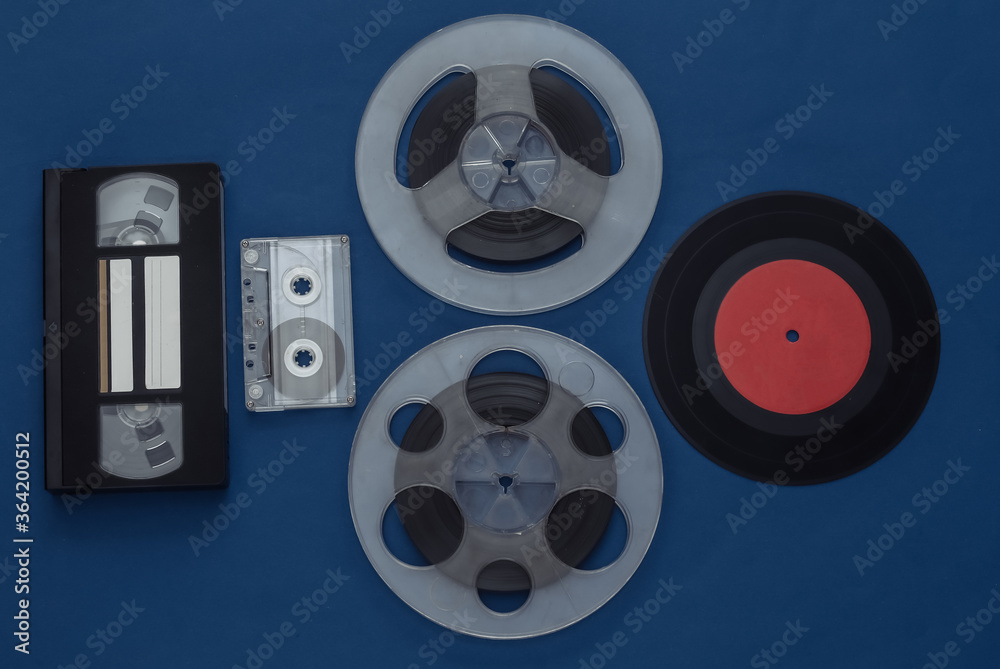Retro flat lay. Audio magnetic tape reel, audio and video cassette, vinyl plate on classic blue background. Top view. 80s