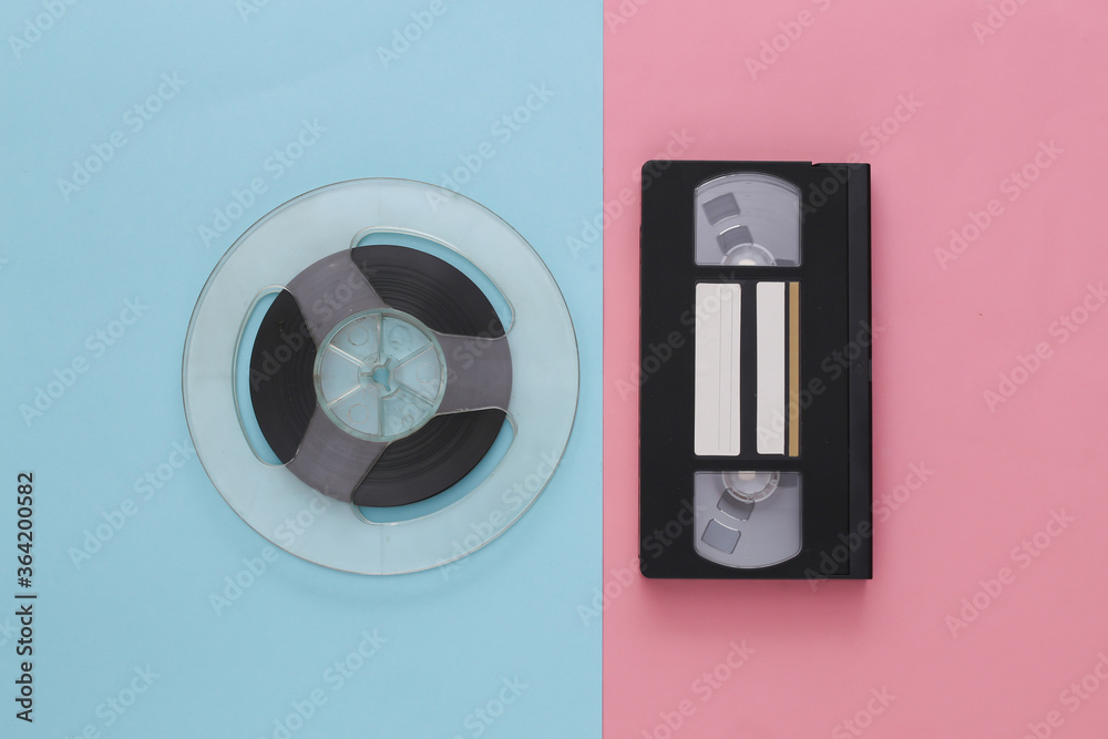 Retro flat lay. Audio magnetic tape reel and video cassette on pink blue pastel background. Top view. 80s