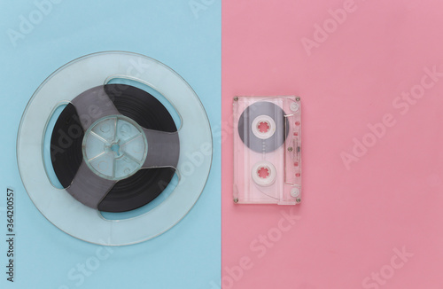 Retro flat lay. Audio magnetic tape reel and audio cassette on pink blue pastel background. Top view. 80s