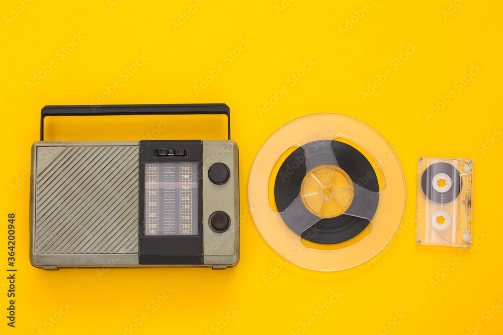 Retro poortable radio receiver and audio magnetic tape reel, audio cassette on yellow background. Top view. Music 80s Retro poortable radio receiver and audio magnetic tape reel, audio cassette on yellow background. Top view. Music 80s