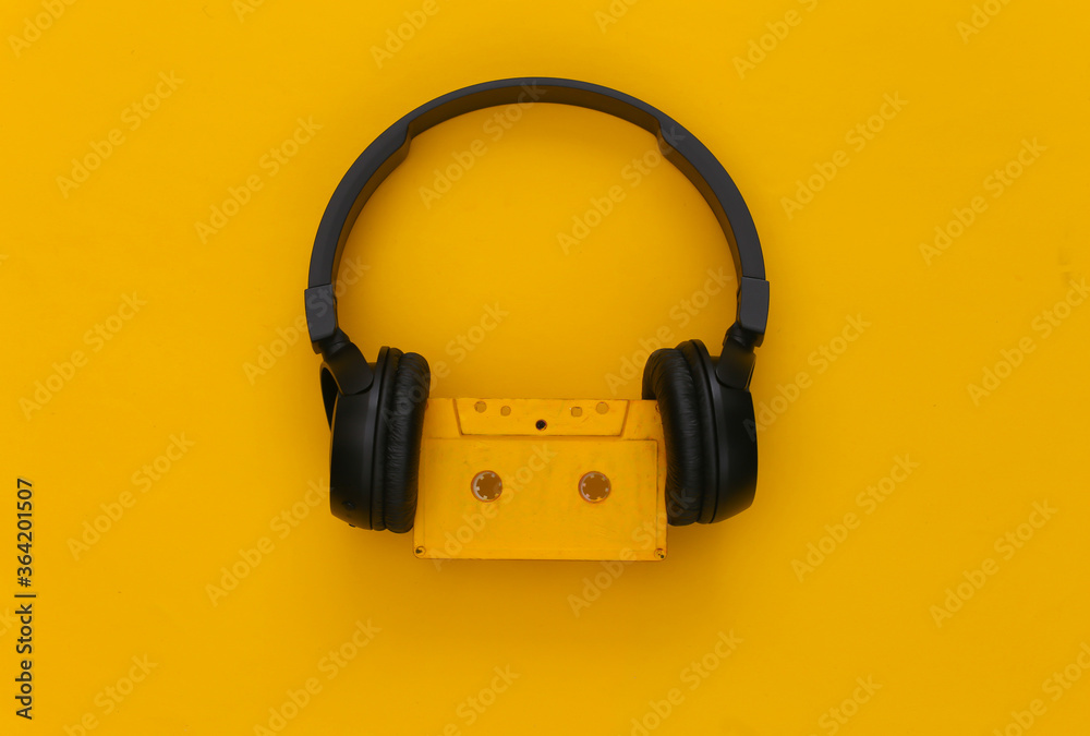 Black stereo headphones with a retro audio cassette on a yellow background. Top view Black stereo headphones with a retro audio cassette on a yellow background. Top view