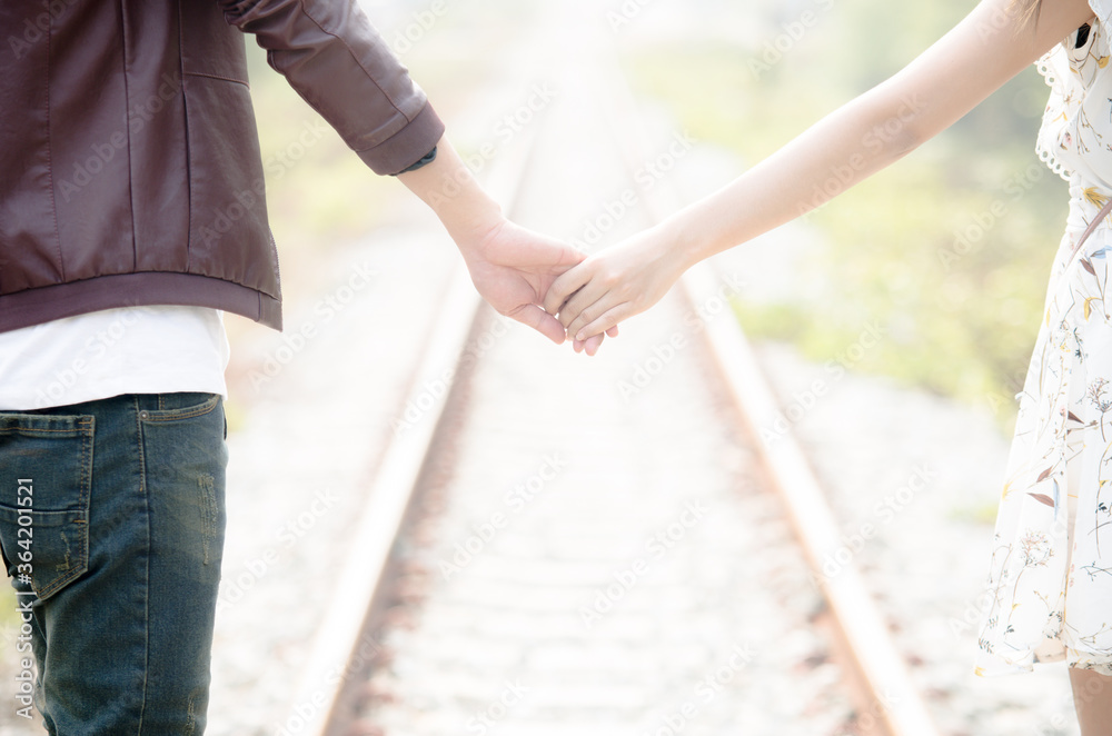 Young loving couple walking hand in hand on railway tracks looking with sunrise background.
