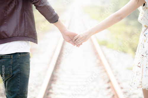 Young loving couple walking hand in hand on railway tracks looking with sunrise background.