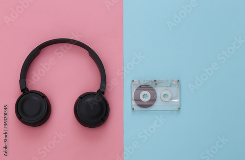 Black stereo headphones with retro audio cassette on pink blue pastel background. Top view