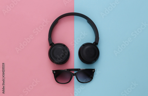 Black stereo headphones and sunglasses on a pink-blue background. Top view